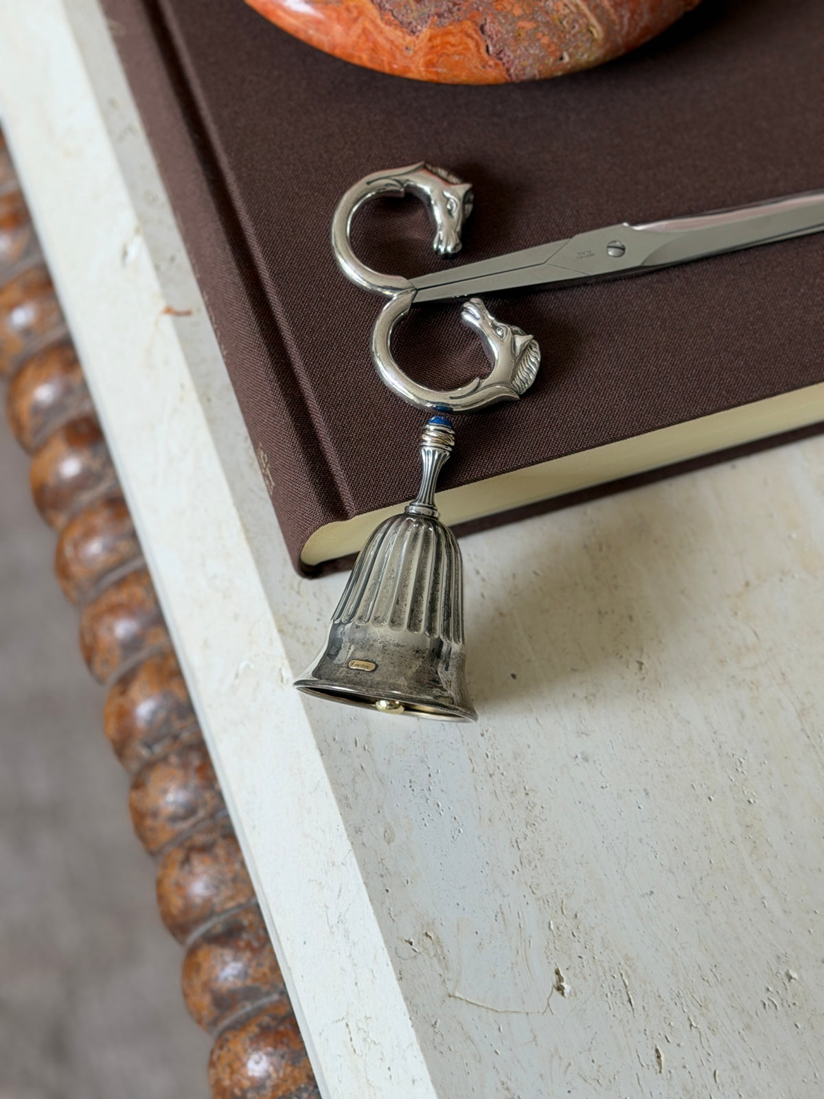 The bell displayed alongside the Hermes horse-head scissors on the same book, with the stone bowl visible above