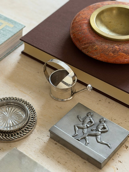 Styled tablescape view of the Cartier vermouth dropper with a pewter box, crystal coaster, and marble dish