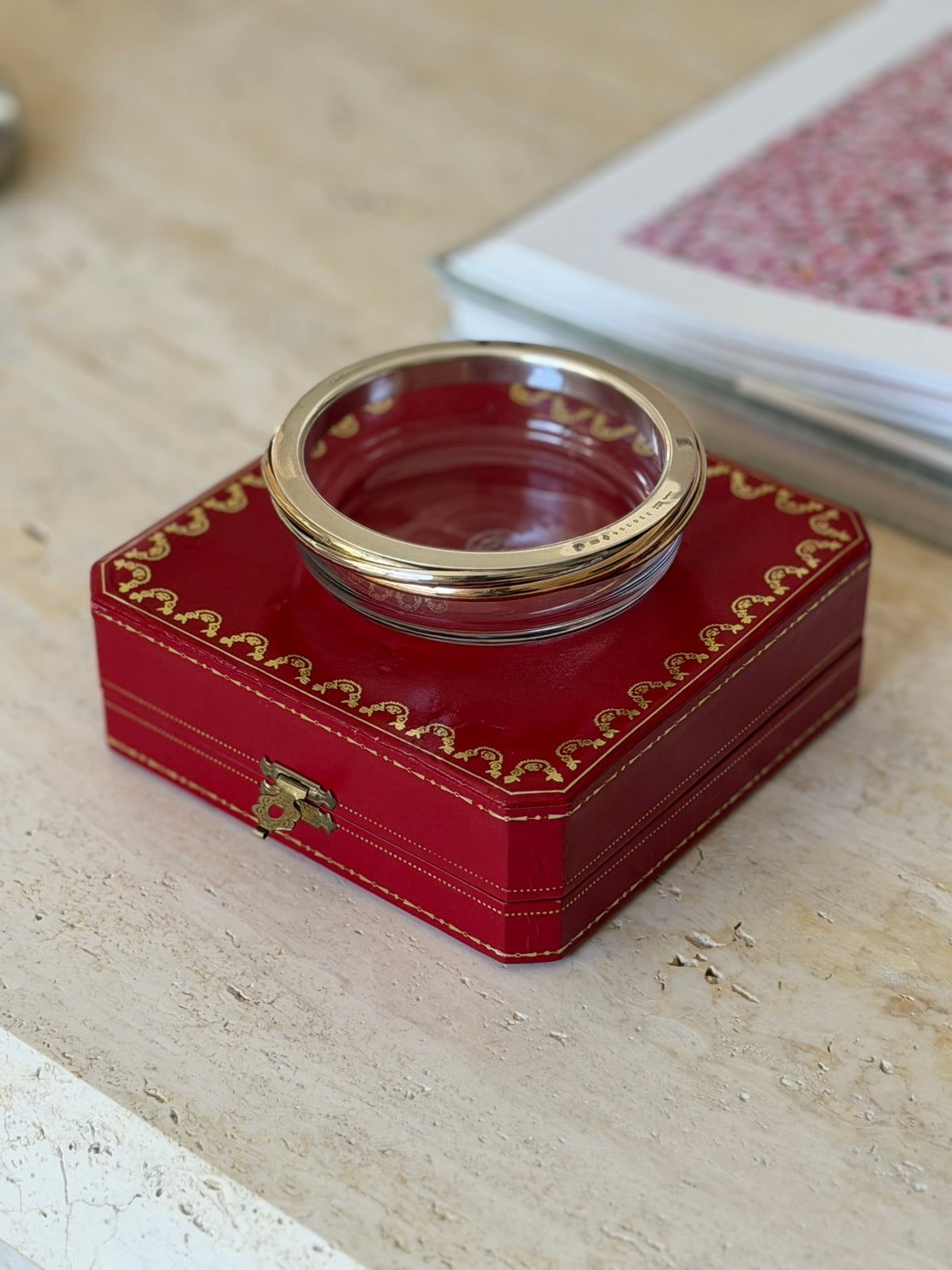 Cartier Trinity crystal dish resting atop its closed presentation box, showing the gold and silver collar encircling the rim