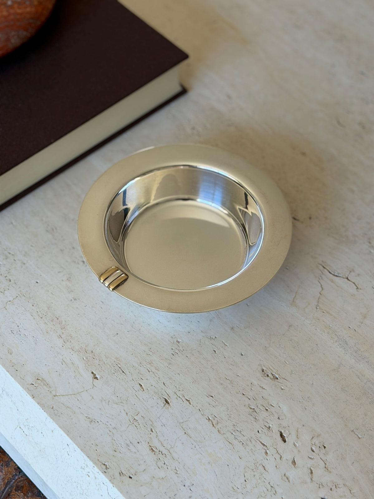 Cartier Trinity sterling silver bottle coaster with a wide flat rim and polished well, a three gold and silver bar detail at the edge, on travertine