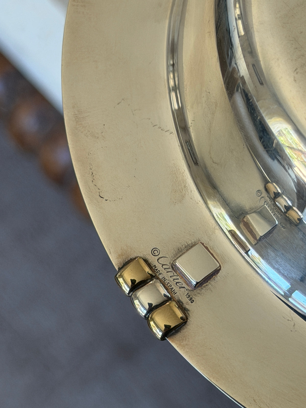 Underside marks on the Cartier coaster, stamped Cartier Made in Spain 1990 beside the Trinity bars and a square hallmark plate