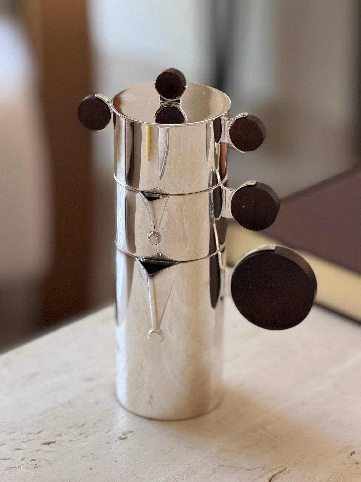 Front view of the Christofle Gigogne nesting coffee service stacked together, silver cylindrical body with rosewood disc handles fanned out
