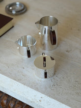 The three pieces of the Gigogne coffee service separated on a stone surface, coffee pot at back with sugar and creamer in front