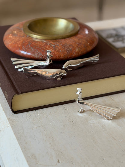 Christofle Gallia peacock and dove knife rests styled on a leather book, four pieces visible