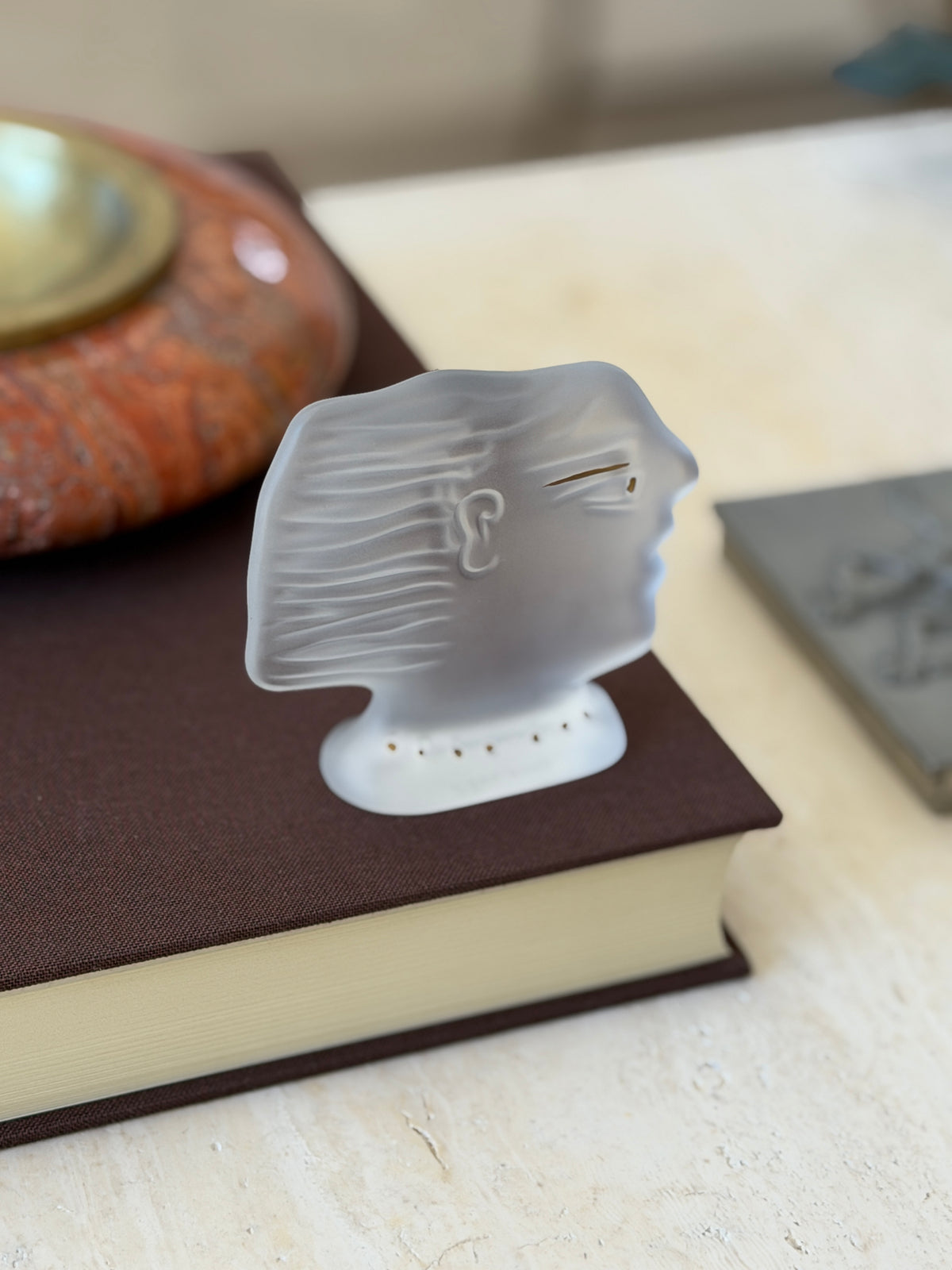 Frosted crystal profile head facing right on a brown book, showing the stylized ear, waved hair, and gold eye line