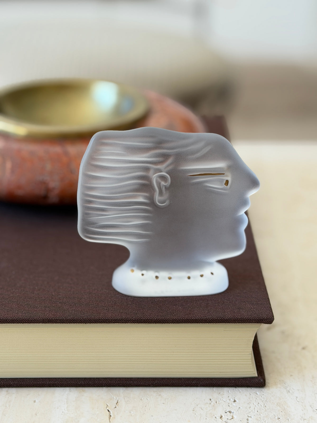 Side profile of the Daum Kalisti sculpture on a book, the satin frosted crystal glowing softly with a row of gold dots at the base
