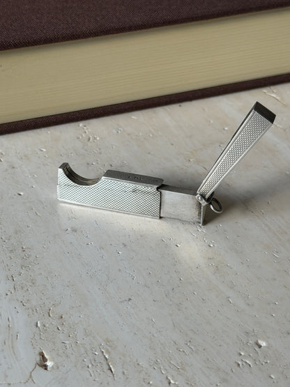 Dunhill cigar cutter opened on travertine, the engine turned lid raised and the curved guillotine slot exposed beside the sliding blade