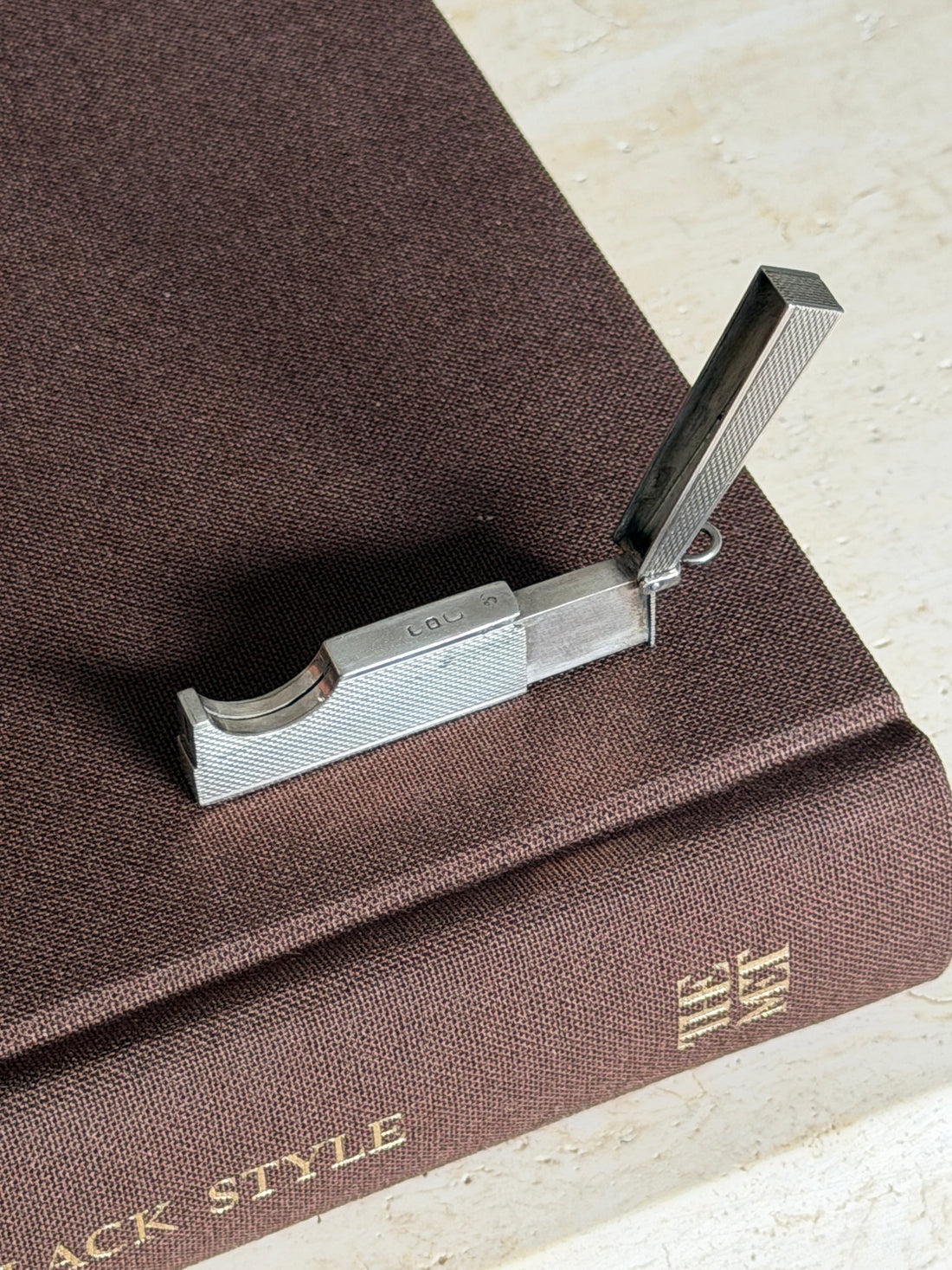 Overhead view of the open Dunhill cutter on a brown book, hallmarks visible along the top edge of the engine turned body