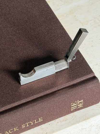 Overhead view of the open Dunhill cutter on a brown book, hallmarks visible along the top edge of the engine turned body
