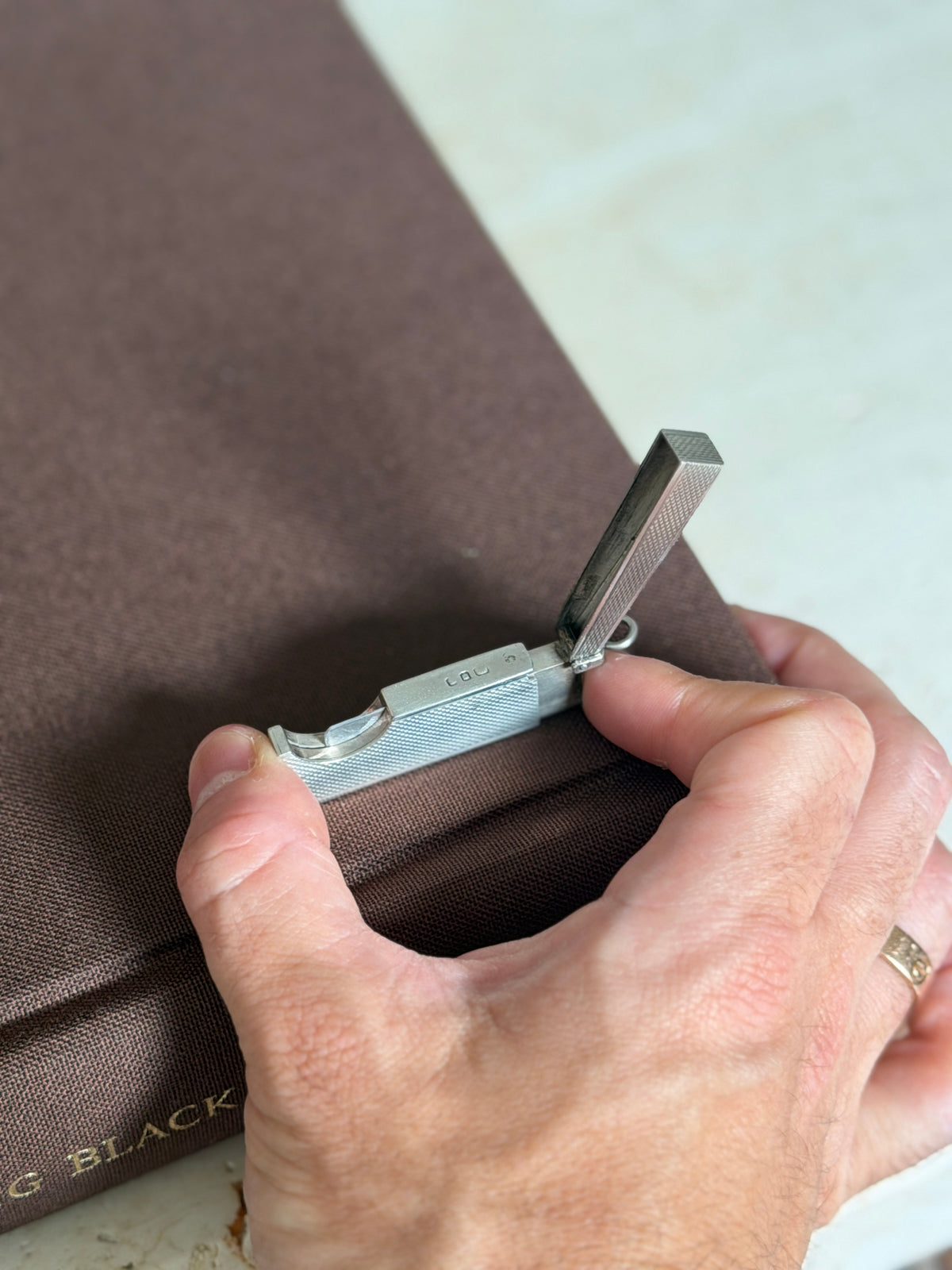 Hand holding the Dunhill travel cigar cutter open, showing its compact scale and the hallmarked silver frame
