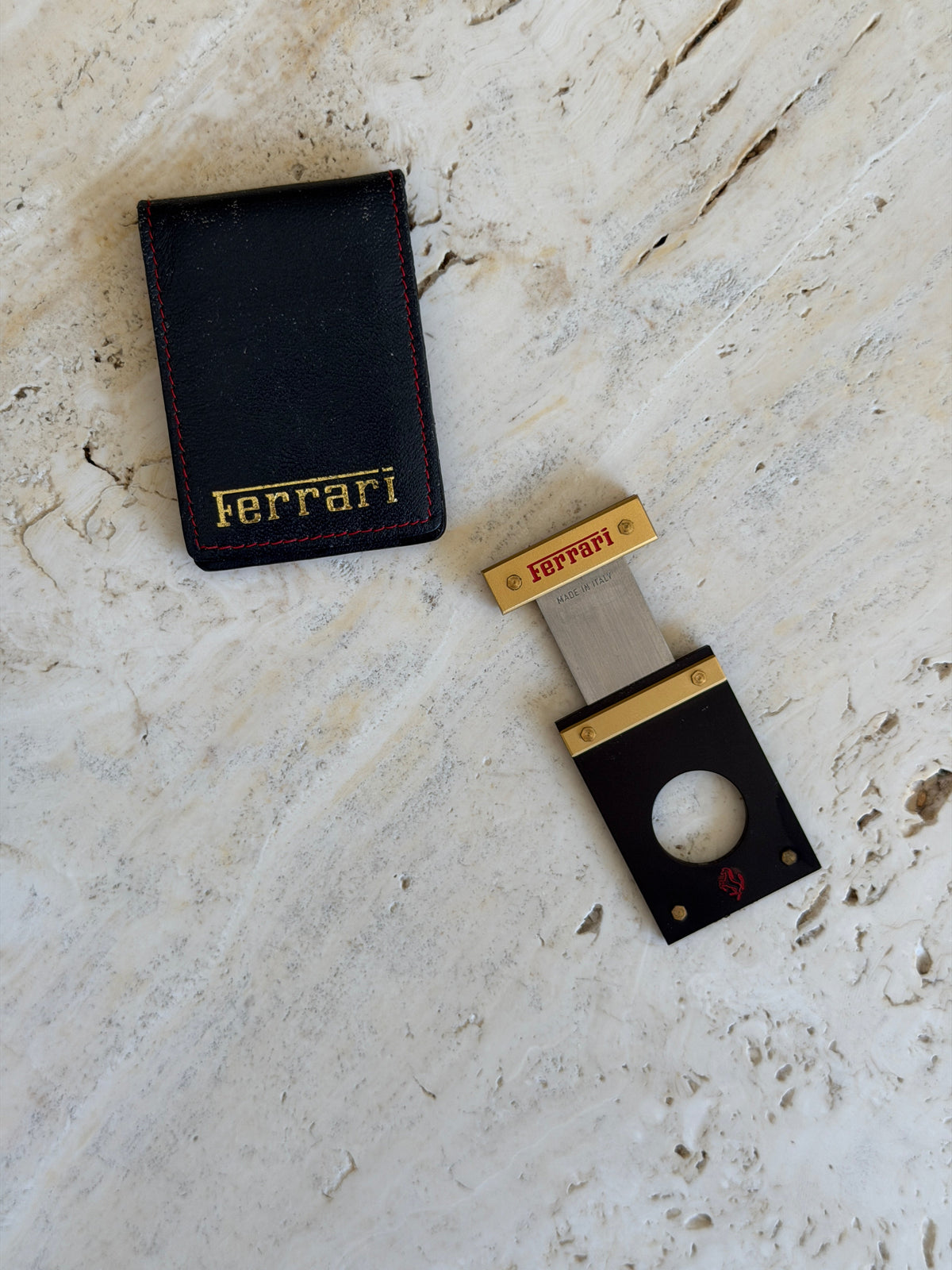 Extended view of the Ferrari cigar cutter with the blade drawn out, beside its pouch