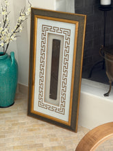 Framed Chinese ruler leaning beside a fireplace next to a turquoise glazed vase holding white blossom branches