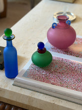 Franco Moretti Murano scavo blue glass bottle with green ball stopper beside a matching green vanity bottle and pink amphora vase on a travertine table