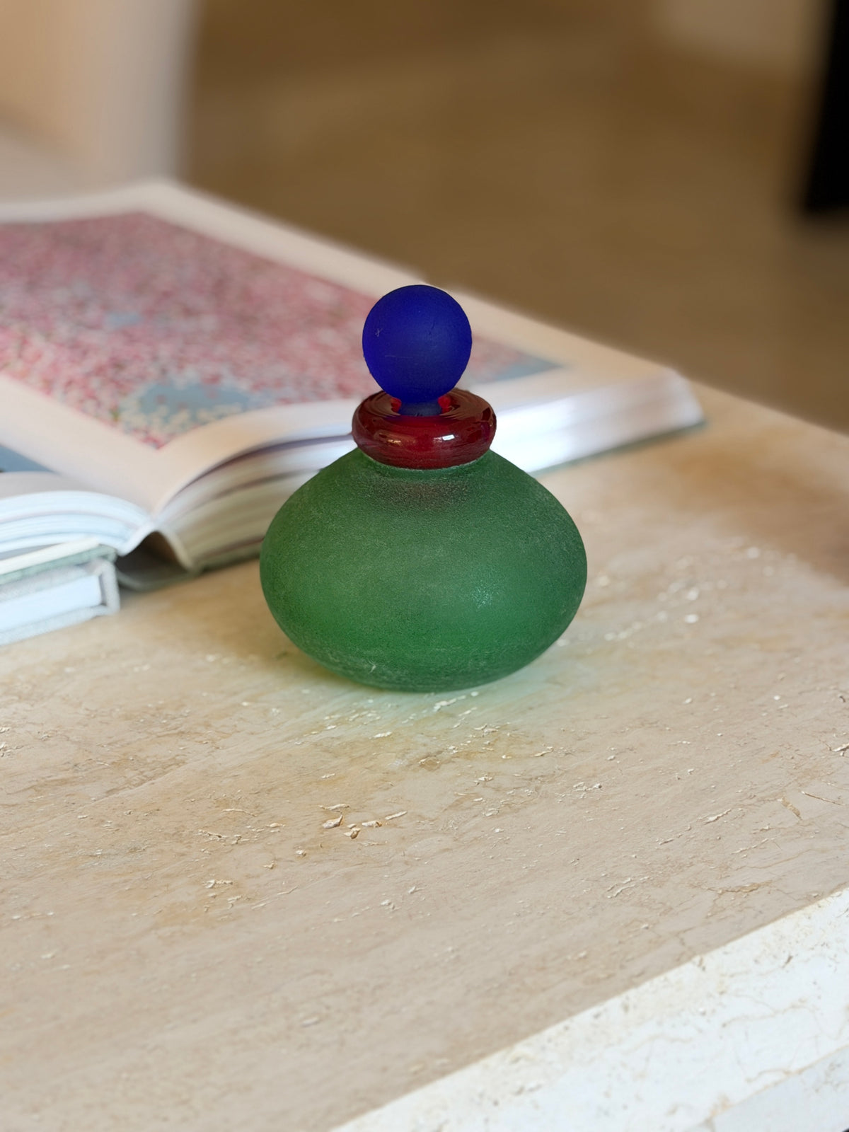 Eye level view of the green scavo vanity bottle showing its flattened round body and frosted, lightly pitted glass texture