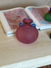 Raspberry pink Murano scavo amphora vase with two cobalt blue scroll handles resting in front of an open art book