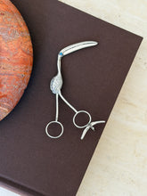 George Unite sterling silver flamingo sugar tongs with a long curved bill, engraved feathers, a turquoise eye, and ring handles, on a brown book
