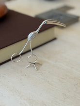 Silver flamingo tongs standing upright on their bird foot stand on travertine, the curved bill reaching forward