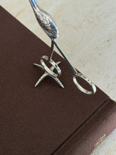 Close view of the flamingo tongs ring handles, both stamped with Birmingham hallmarks, above the textured foot stand