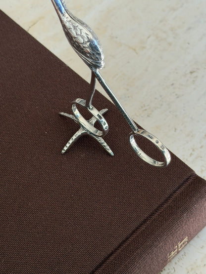 Close view of the flamingo tongs ring handles, both stamped with Birmingham hallmarks, above the textured foot stand