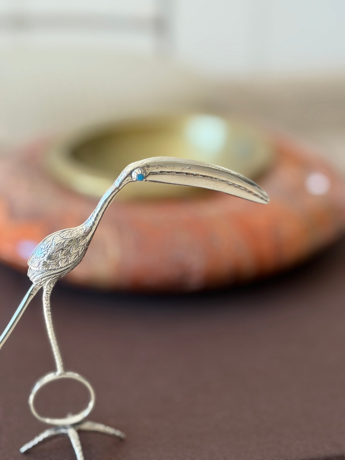 Detail of the flamingo head with its turquoise set eye and finely chased feathered body, a red stone ashtray blurred behind