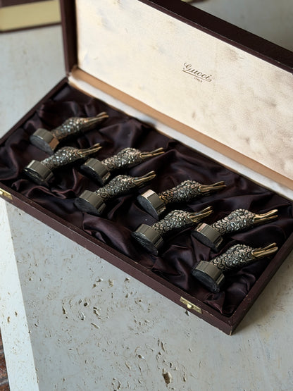 Angled view of the open Gucci box on travertine, eight duck heads in two staggered rows with polished collars and gilt bills