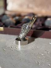 Single Gucci duck head place card holder standing upright on travertine, the open gilt beak and engraved plumage in focus with the box behind