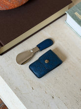Overhead view of the folded Gucci shoehorn resting beside its blue leather case