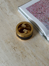 Overhead view from another angle showing the leather band and brass G motif with the floral book nearby