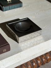 Gucci vide poche with a black stone square top and round dished well, its silver sides engraved with a repeating interlocking G pattern, on travertine