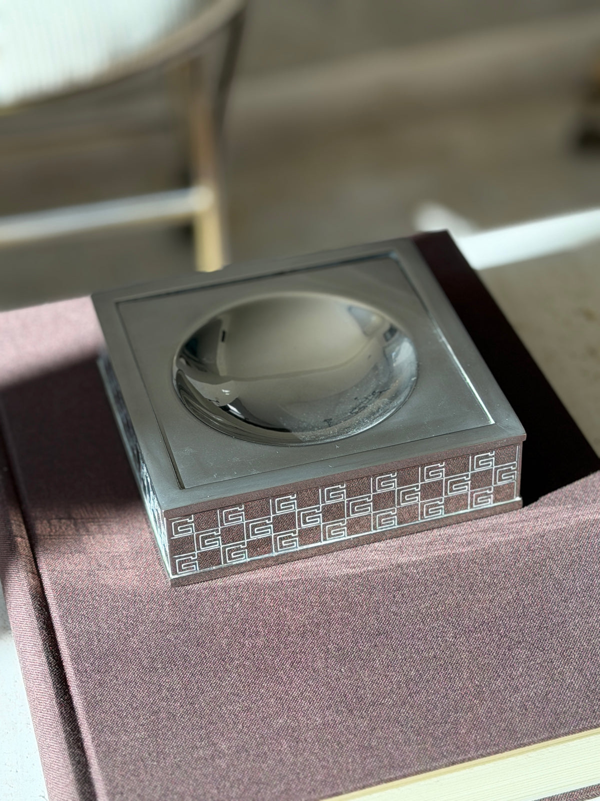 Overhead view of the square Gucci vide poche on a brown book, the satin black top framing the glossy round well