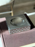 Overhead view of the square Gucci vide poche on a brown book, the satin black top framing the glossy round well