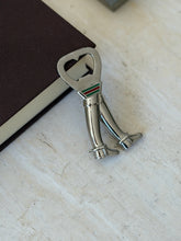Gucci bottle opener leaning against a brown book on travertine, the boots standing side by side below the web stripe collar