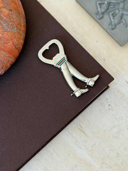 Overhead view of the Gucci riding boots opener lying on a brown book, the boots striding beneath the heart shaped cap lifter