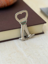 Gucci bottle opener standing upright against a book edge, showing the cap lifter opening and enamel green red green stripes