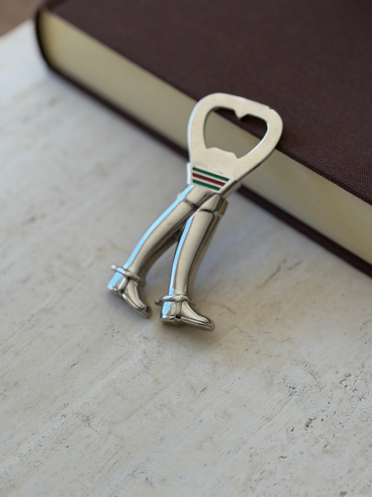 Close view of the Gucci riding boot opener propped on travertine, detailing the spurs, ankle straps, and polished silver boot shafts