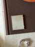 Closed folding frame resting on a fabric-bound book, showing the engine-turned silver panel and vermeil border