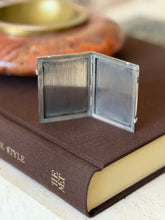 The frame opened into its book-like stance, showing the tarnished silver photo backing inside both panels