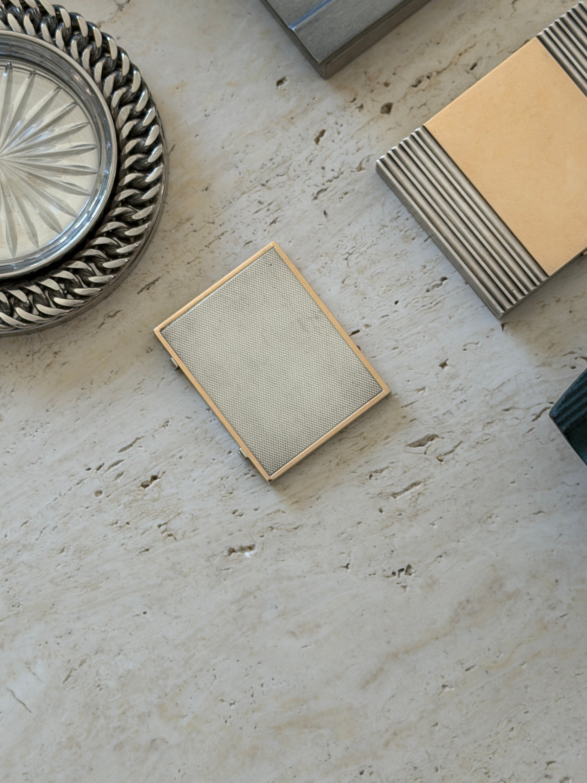 The closed frame photographed on a stone surface next to a silver woven-rim coaster and another framed object