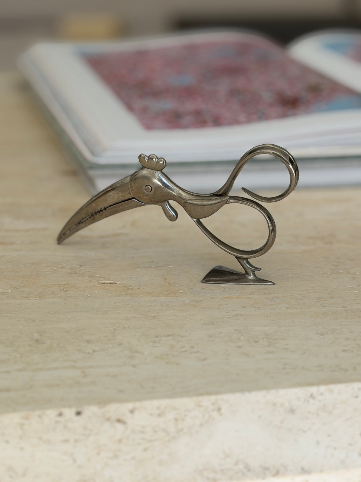 Eye level profile of the Art Deco parrot tongs highlighting the curved serrated beak and figure-eight loop handles above the angular foot