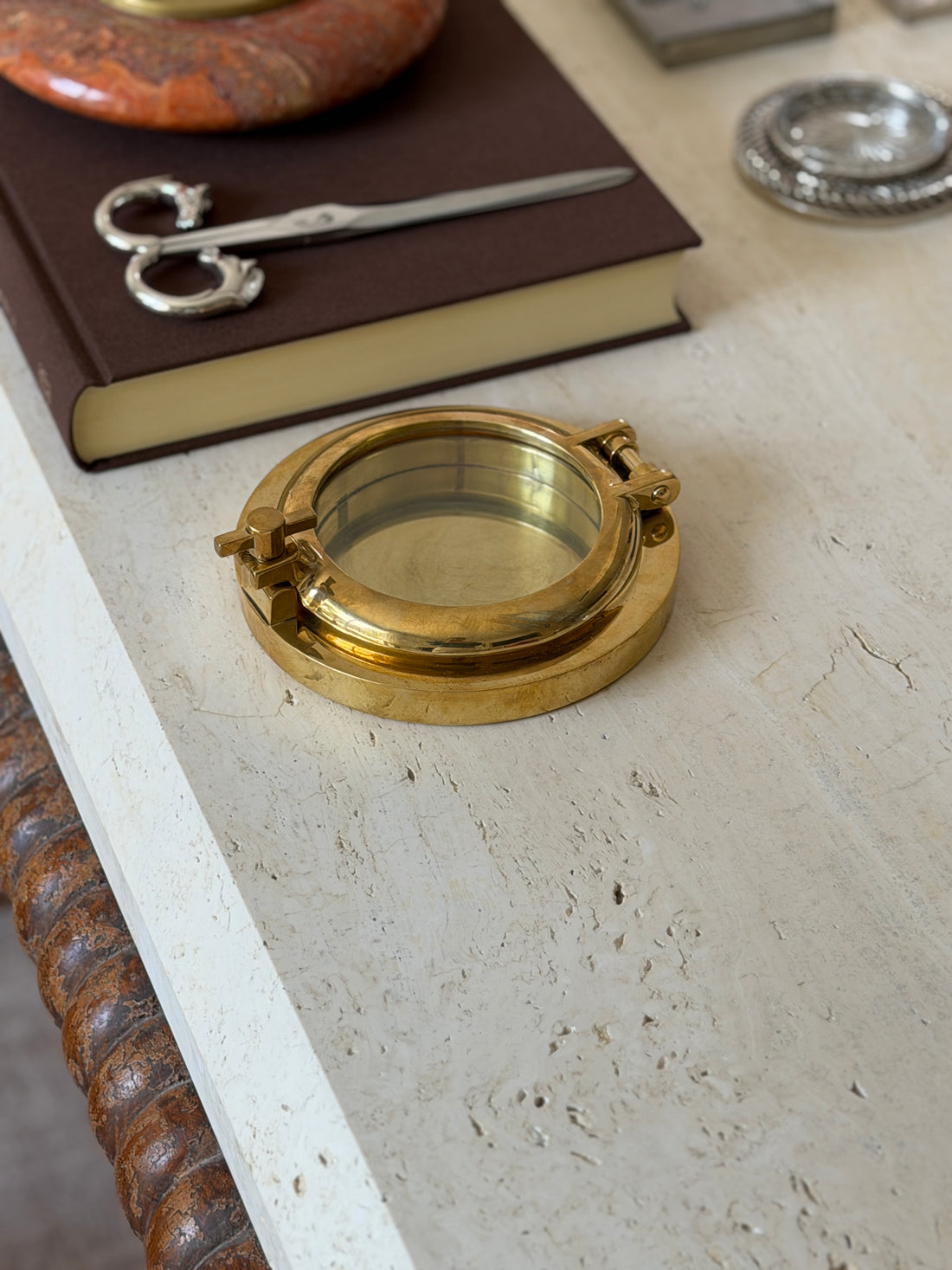 Another angle of the closed porthole box showing the glass front and hinge, with the same book and desk objects nearby