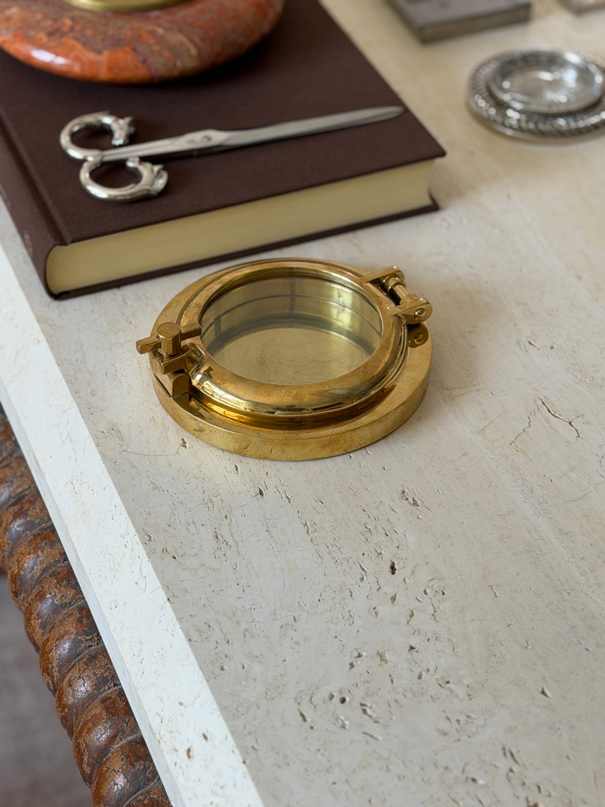 Another angle of the closed porthole box showing the glass front and hinge, with the same book and desk objects nearby