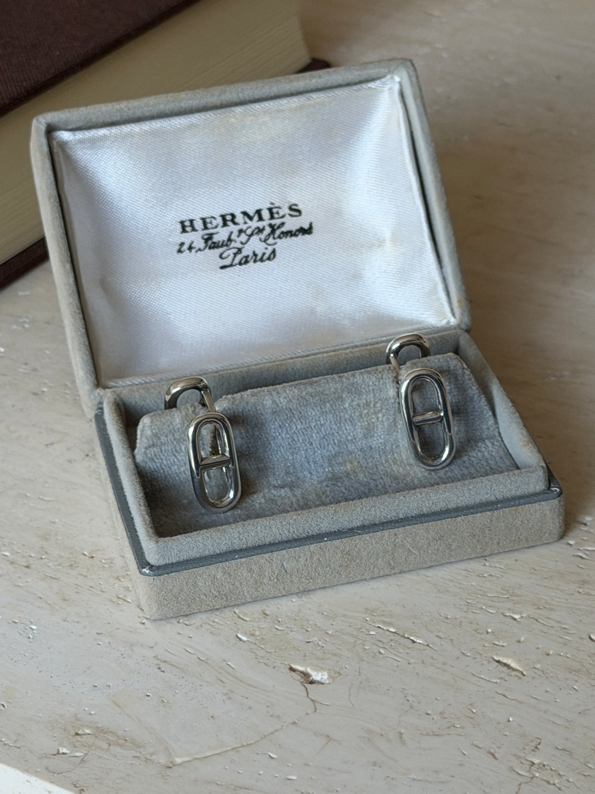 Pair of Hermes anchor chain link cufflinks seated in the gray suede presentation box, polished silver catching the light