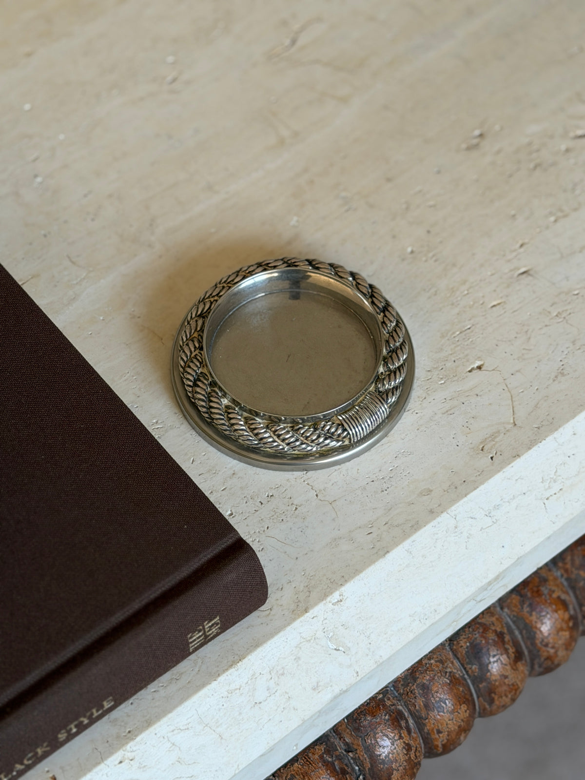 Hermes Cordage rope coaster from France viewed at an angle with the rope binding turned to the front, beside a brown book on a travertine surface