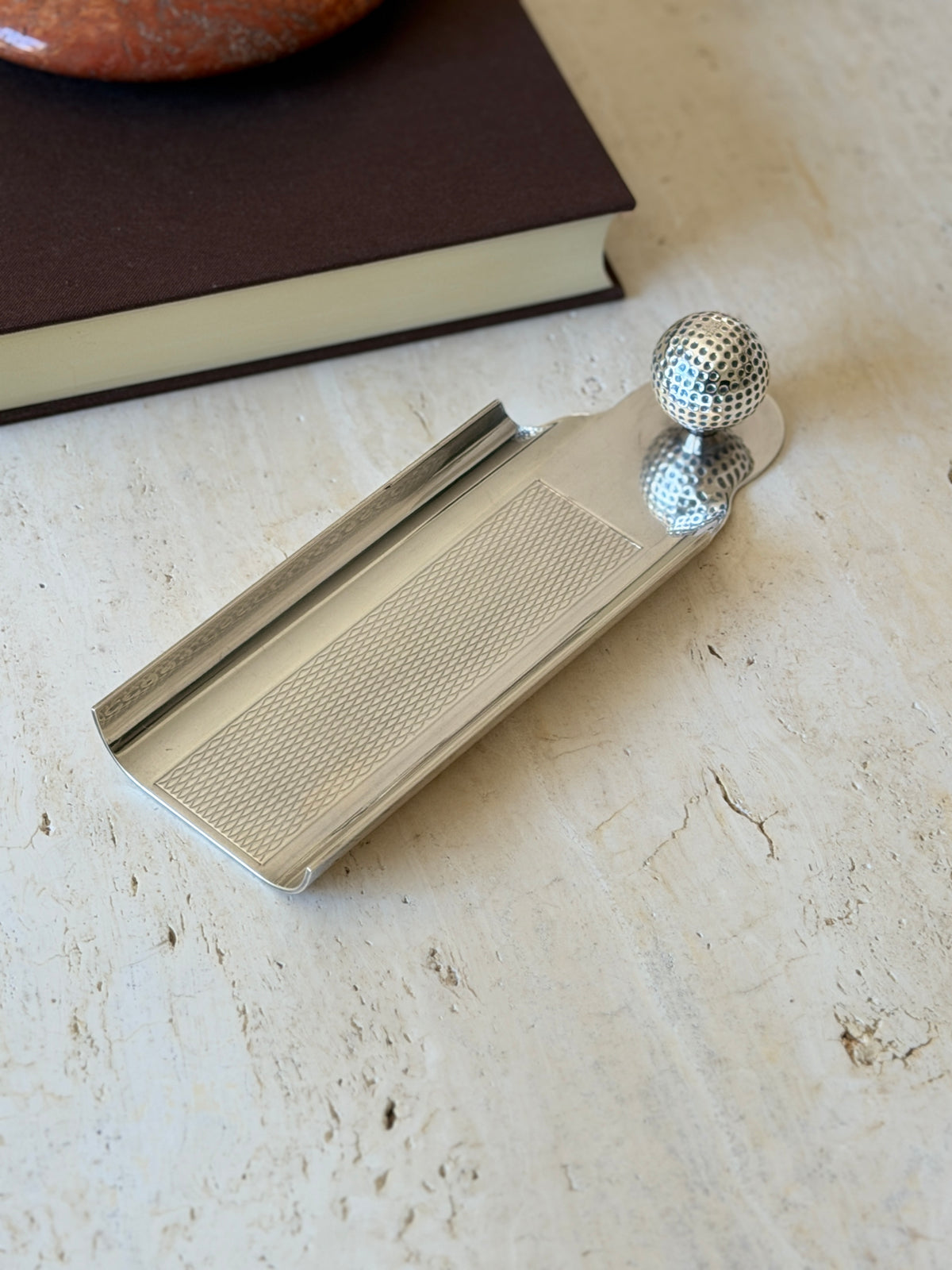Angled view of the Hermes golf ball desk tray, its curled rolled edges and guilloche panel reflecting soft light