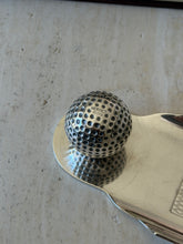 Close up of the dimpled silver golf ball on the Hermes tray, stamped HERMES PARIS on its top