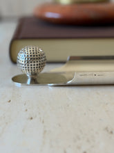 Low eye level view of the Hermes tray edge stamped HERMES PARIS and Made in France, the golf ball rising at the end