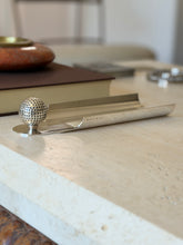 Side profile of the Hermes golf ball desk tray on a travertine console, a red stone ashtray and brown book behind