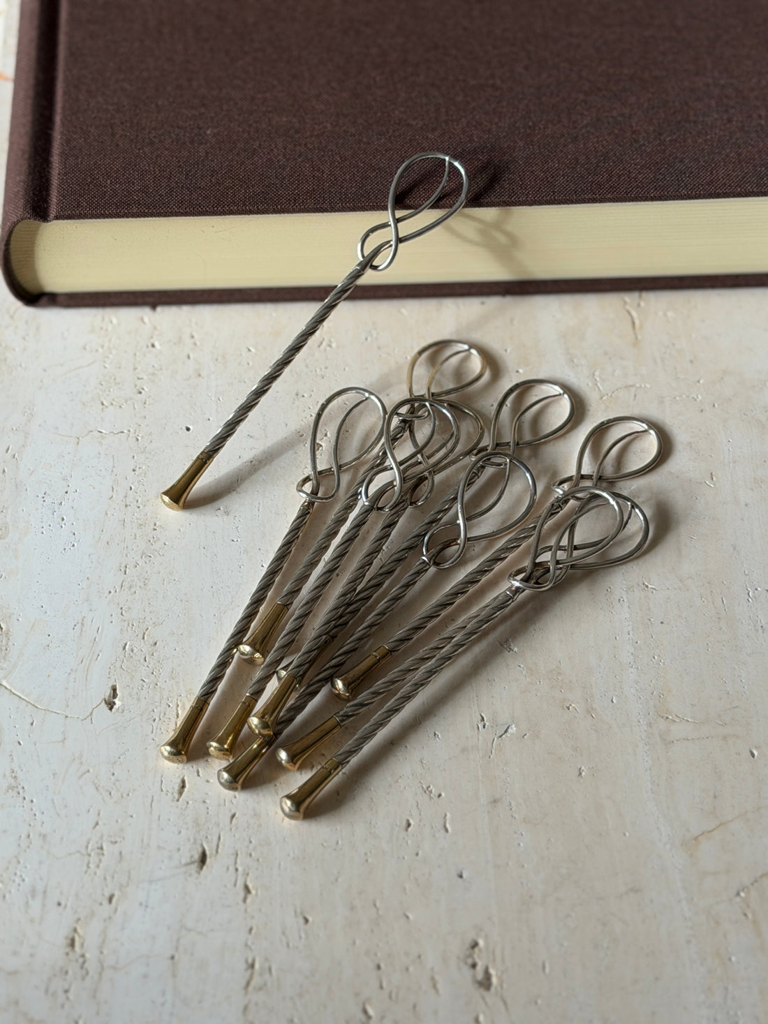 Hermes cocktail stirrers grouped on travertine, the twisted silver stems ending in flared gilt tips, one propped on a book edge