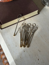 Hermes gilt and silver stirrers on a travertine console beside a brown book, a silver coaster in the corner