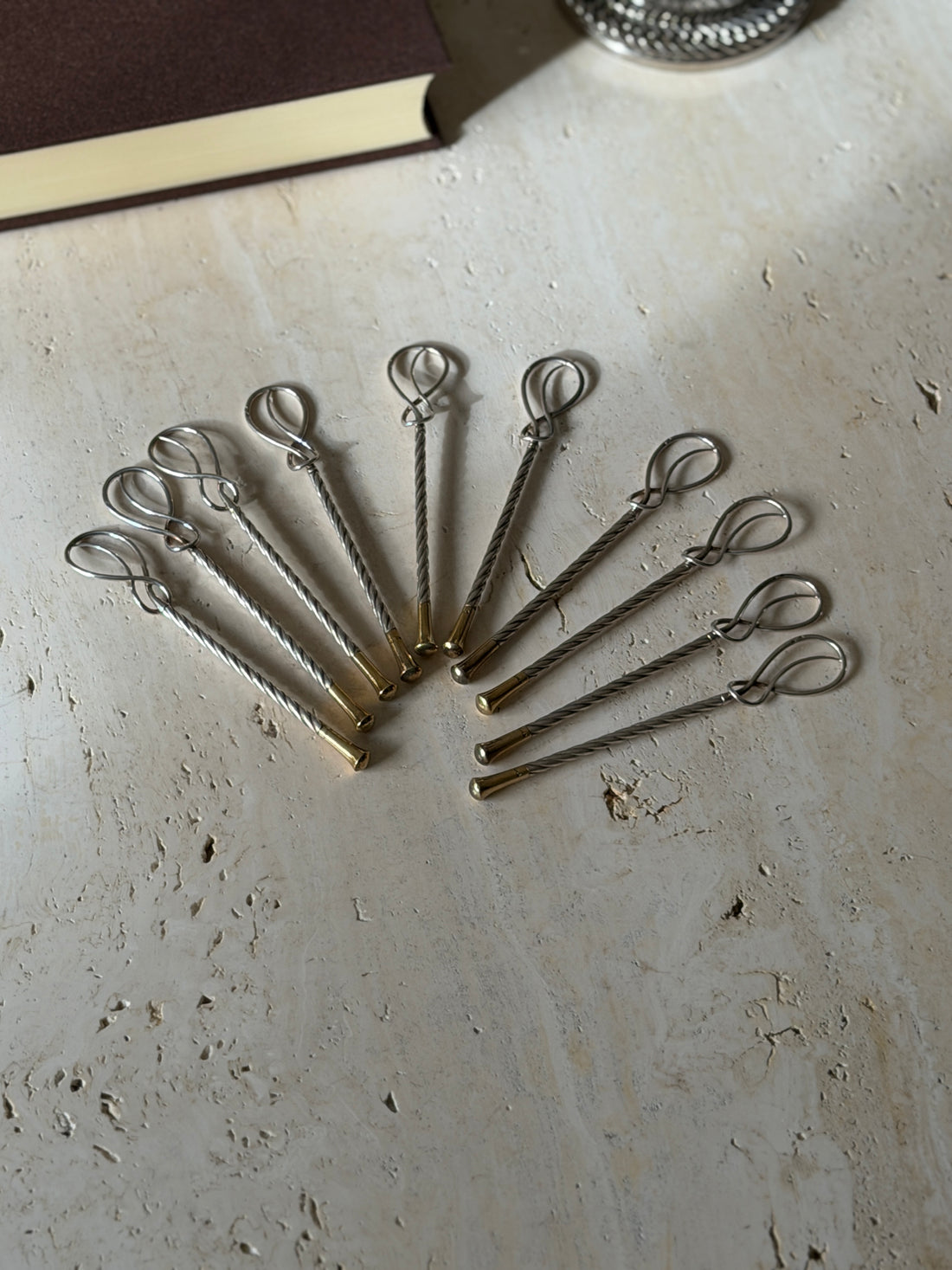 Ten Hermes champagne stirrers fanned out on travertine, figure eight loop tops above twisted silver stems and gilt tips